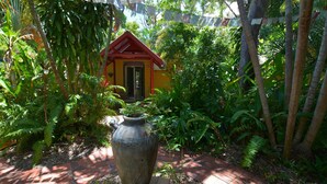 A small red-roofed structure surrounded by lush greenery, a large stone planter in the foreground, and a brick pathway leading to the structure. - Shambhala Retreat Cottages a peaceful place intended for rest and relaxation. (Nelly Bay)
