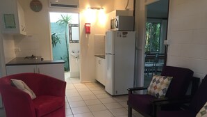 A compact living space with a kitchenette, a red armchair, a purple sofa, and a dining area visible through an open doorway. - Shambhala Retreat Cottages a peaceful place intended for rest and relaxation. (Nelly Bay)