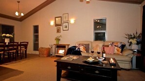 A cozy living room with a fireplace, a sofa, a coffee table, and a dining area with chairs. - Much loved holiday chalet (Ohakune)