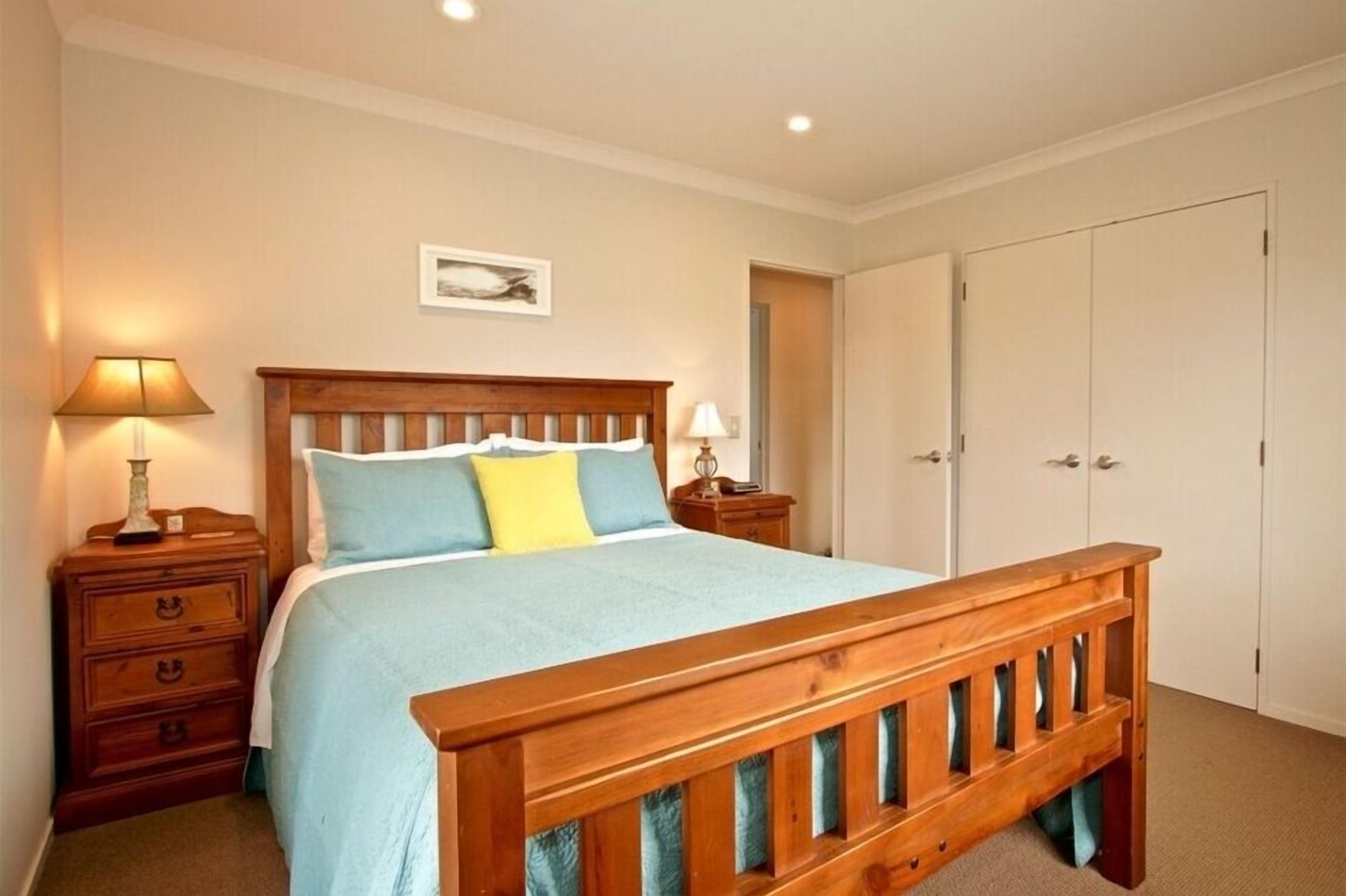 A bedroom with a wooden bed, two bedside tables with lamps, a wardrobe, and a framed picture on the wall.
