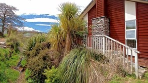 A red house with a stone chimney, surrounded by various plants and a small stream. - Much loved holiday chalet (Ohakune)