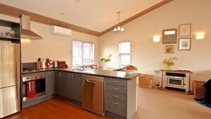 A modern kitchen with a central island, stainless steel appliances, and a dining area with a small table and chairs. - Much loved holiday chalet (Ohakune)