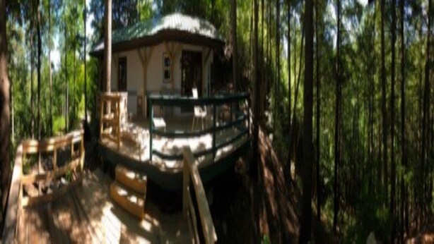 Una cabaña con terraza, rodeada de bosque.