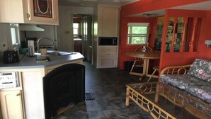 Cocina compacta con lavamanos, estufa y microondas. Hay una zona de comedor con mesa y sillas, además de un sofá con tapicería floral.