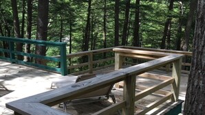 Una terraza de madera con bancos y barandillas, rodeada por un bosque.