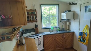 A kitchen with wooden cabinets, a stove, a microwave, and a window with a view of greenery. - Rose Cottage get-away, Foxton Beach (Foxton Beach)