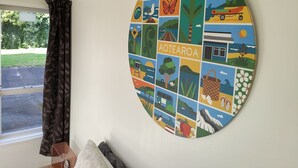A round wall art piece with various illustrations, including a train, a butterfly, and a mountain. - Rose Cottage get-away, Foxton Beach (Foxton Beach)