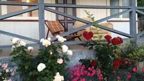 A covered outdoor seating area with a wooden table and chairs, surrounded by various flowering plants. - Rose Cottage get-away, Foxton Beach (Foxton Beach)