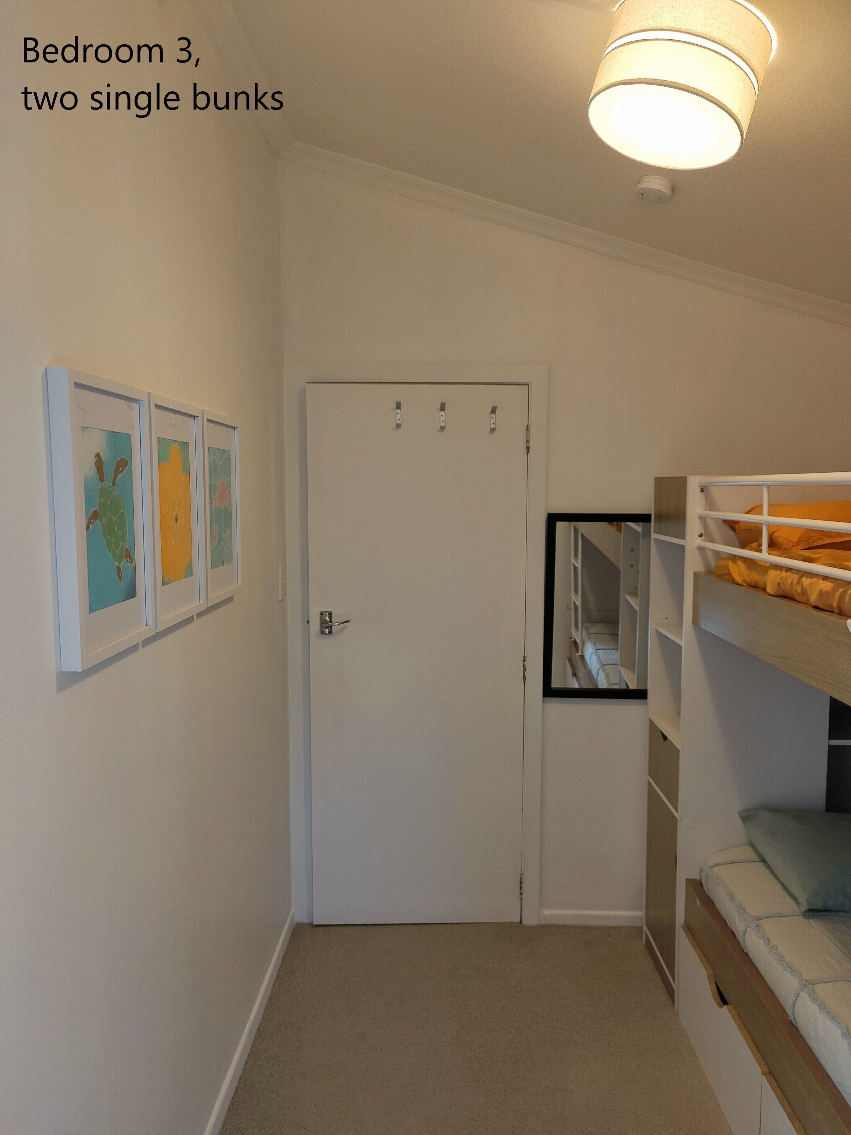 A bedroom with two single bunk beds, a door with a handle, and three framed pictures on the wall.