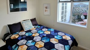 A bedroom with a large bed, a window with a view of the backyard, and a ceiling light. - Rose Cottage get-away, Foxton Beach (Foxton Beach)
