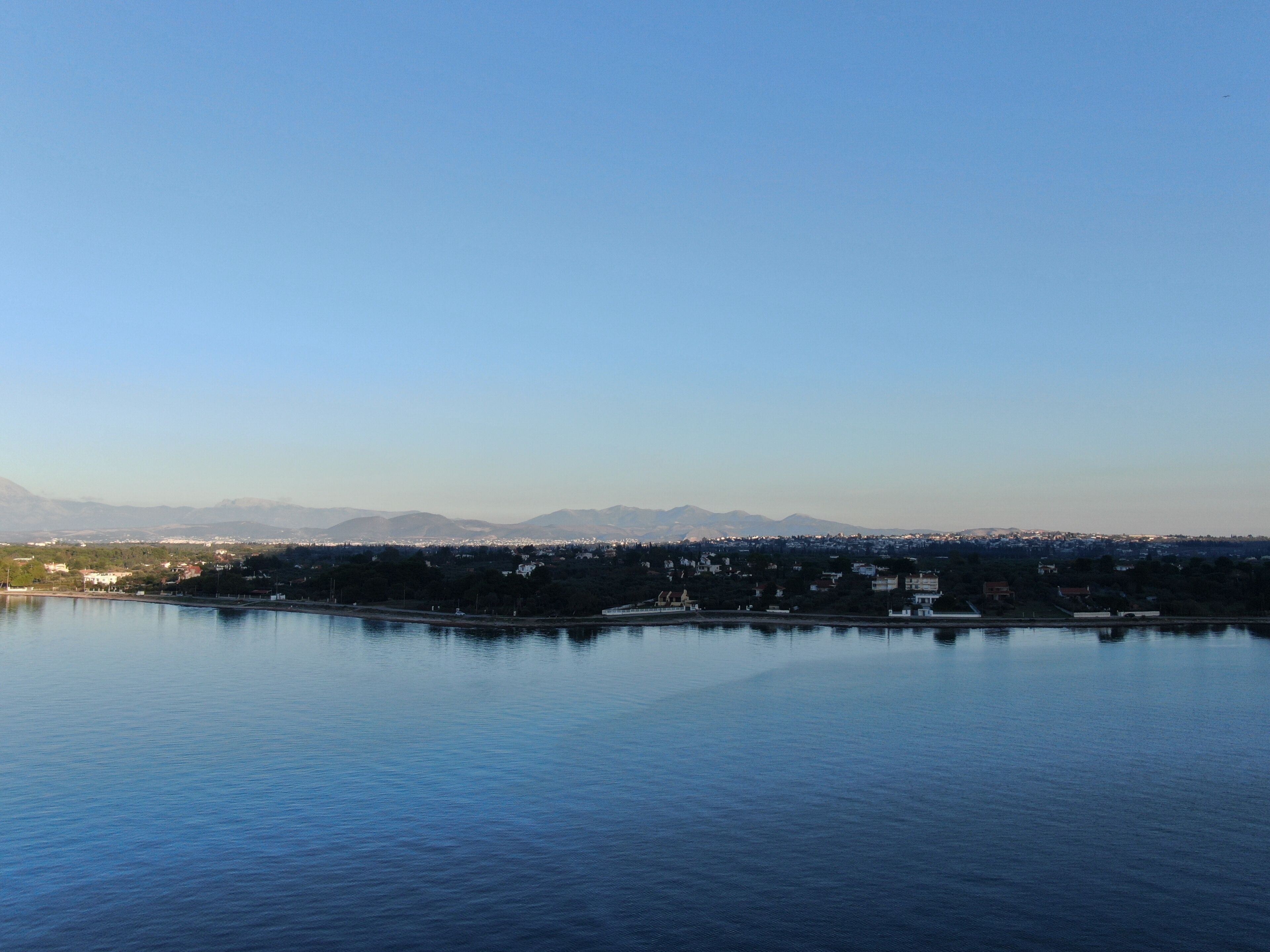Ruhige Wasserfläche mit einer fernen Stadtlandschaft und Bergen.