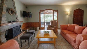 A living room with a fireplace, seating, a television, and a view through a glass door. - Seafront cottage with orchard and garden (Drosia)
