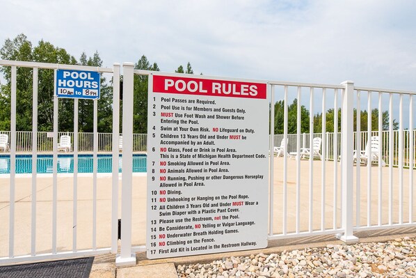 A pool area with a sign listing pool rules and hours.