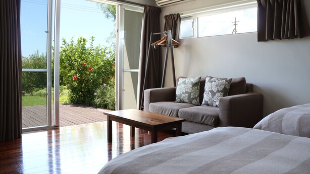 Una habitación con sofá, cama, mesa de madera y puerta corrediza de vidrio que da a una terraza exterior.