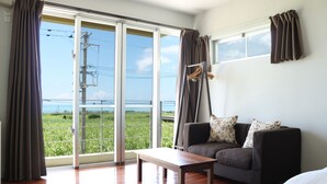 Una habitación con sofá, mesa y vistas a un campo verde a través de amplias ventanas.