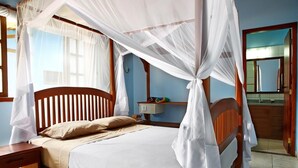 Quarto com cama de madeira, roupa de cama branca, mesa de cabeceira e janela com cortinas.