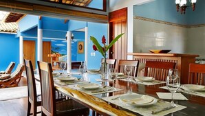 Uma sala de jantar com uma mesa de madeira comprida posta para uma refeição, cercada por cadeiras de madeira.