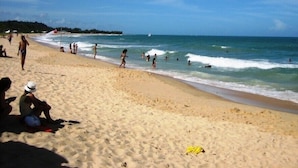 Uma praia arenosa com pessoas nadando e caminhando pela orla.