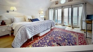A bedroom with a bed, a nightstand, a desk, a ceiling fan, and a large window with a view of the sea. - Beachfront 3-bedroom vacation home just 14 minutes from Yale University (Milford)