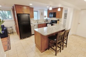 Una cocina moderna con armarios de madera, un refrigerador negro, encimeras de granito y una isla central con taburetes de bar.