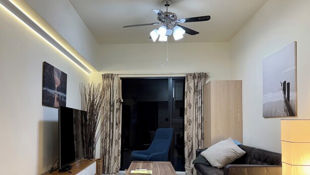 A modern living room with a ceiling fan, a flat-screen TV, a wooden coffee table, a sofa, and a chair. - Modern Building in City Center 3/2bath across Taipei Main Station (Taipei City)