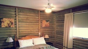 Ein schläfriger Raum im Chalet-Stil mit Bett, zwei Nachttischlampen, Deckenventilator und Wandkunst.