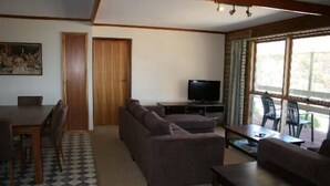 Ein Wohnzimmer mit Sofa, Fernseher, Esstisch und Stühlen.