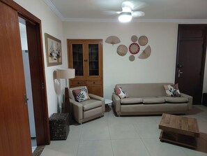 A living room with a sofa, armchair, wooden cabinet, and decorative wall hangings.