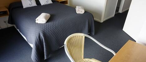 Habitación de hotel con una cama grande, dos almohadas con diseños de caballitos de mar, una lámpara de noche, una silla y una pequeña mesa.