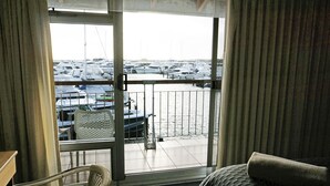 Ett hotellrum med en balkong som vetter ut mot en småbåtshamn med båtar.