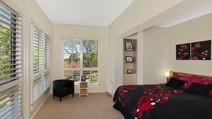Une chambre à coucher avec un lit, une chaise, une étagère avec des photos et une fenêtre avec des stores.