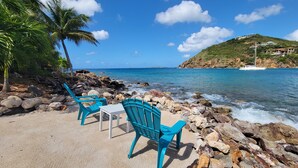 A beachside seating area with a table and chairs, rocky shoreline, and a view of the ocean and distant hills. - Pet friendly. Kayak, paddle board, snorkel, or hike to the beach. (Cruz Bay)