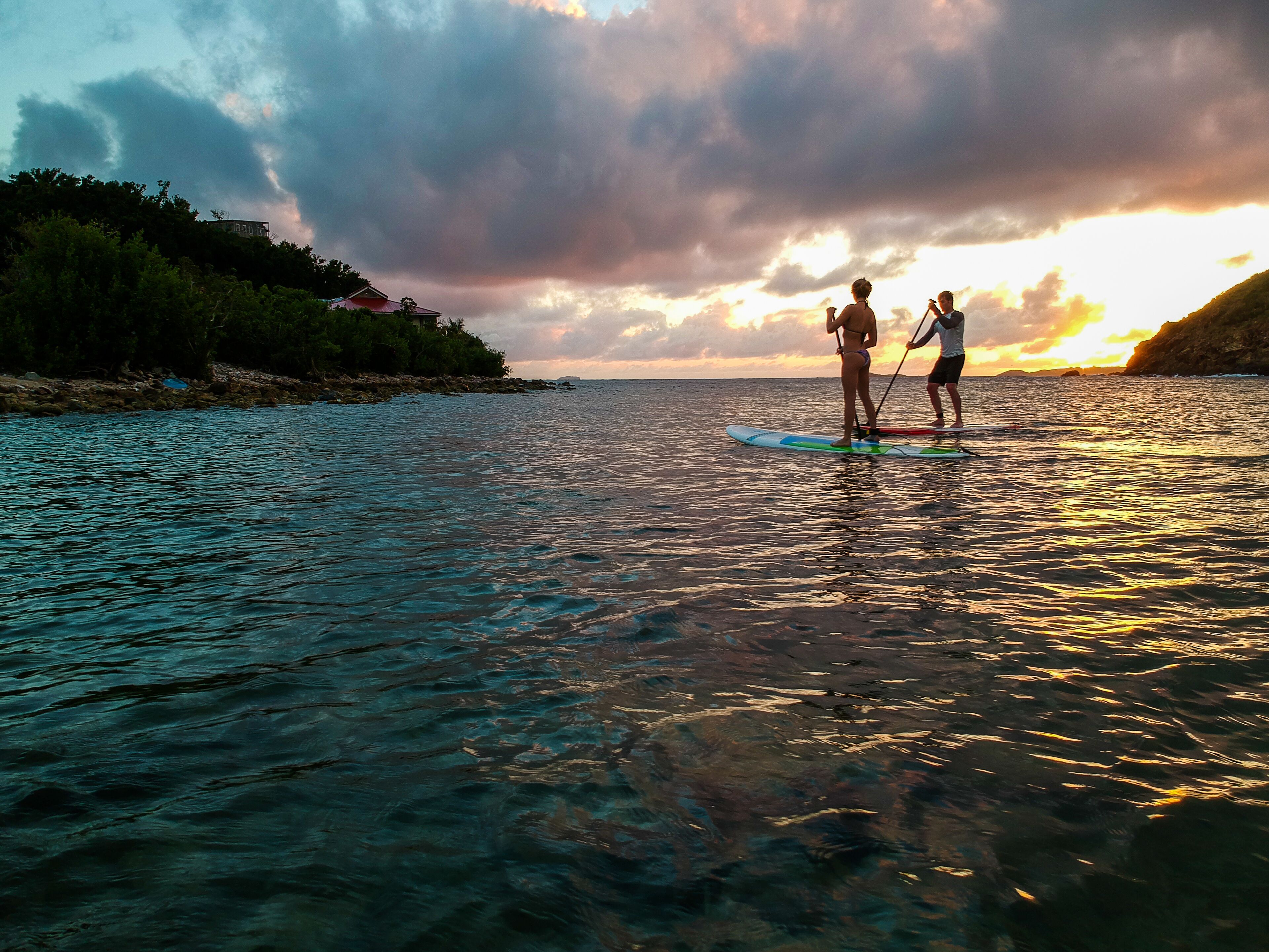 Dos personas haciendo paddleboard sobre un agua tranquila con un atardecer al fondo.