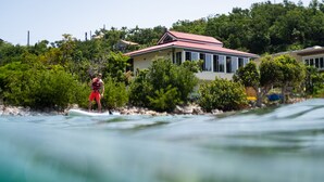 A coastal house with a red roof, surrounded by lush greenery and located near a body of water. - Pet friendly. Kayak, paddle board, snorkel, or hike to the beach. (Cruz Bay)