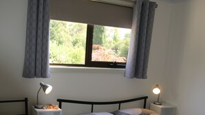 A bedroom with two single beds, a window with curtains, bedside lamps, and a small table with a lamp. - ALTONA GARDEN RETREAT (spreyton)