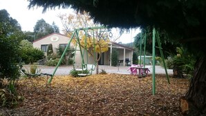 A playground with swings and a slide, surrounded by trees and a building in the background. - ALTONA GARDEN RETREAT (spreyton)