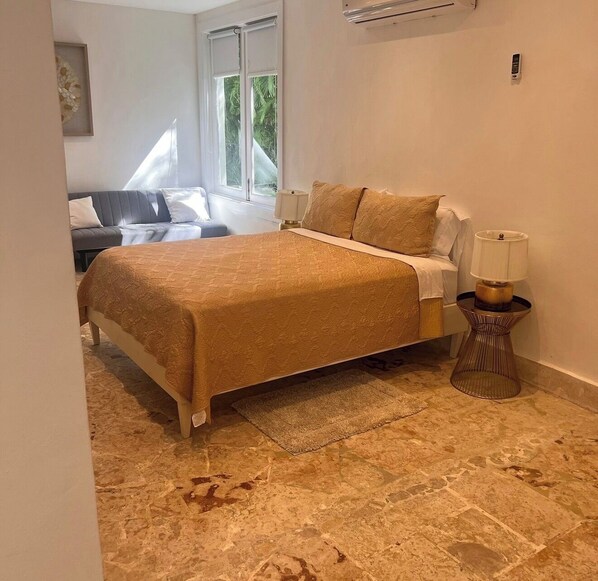 A bedroom with a bed, a bedside table with a lamp, a window with blinds, and a wall-mounted air conditioning unit. - High standard luxury villa (Higuey)