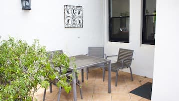 An outdoor patio with a table and two chairs, a potted plant, and a decorative metal piece on the wall.