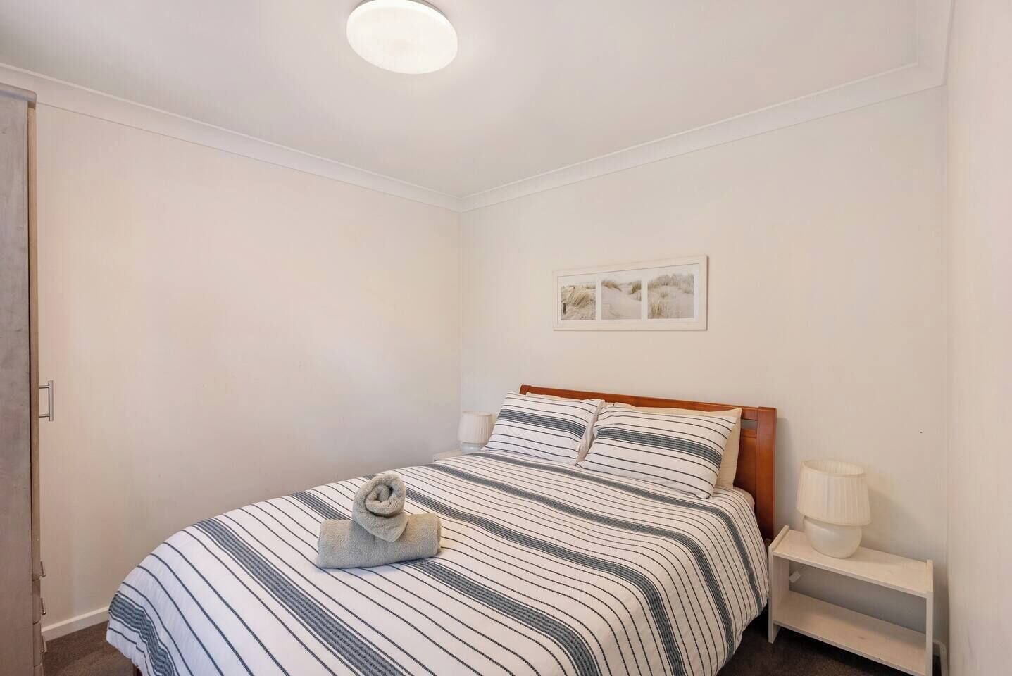 Une chambre à coucher avec un lit, une table de chevet, une lampe et un tableau encadré au mur.