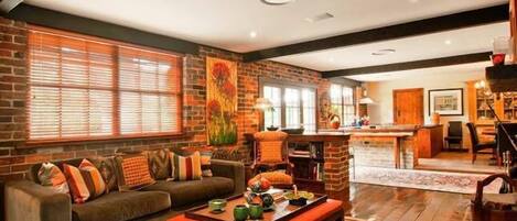 A cozy living room with a brick wall, a sofa, a coffee table, and a kitchen area in the background.