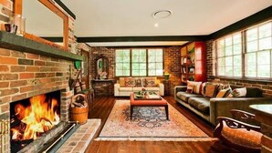 A cozy living room with a brick fireplace, a sofa, a coffee table, and a large window.