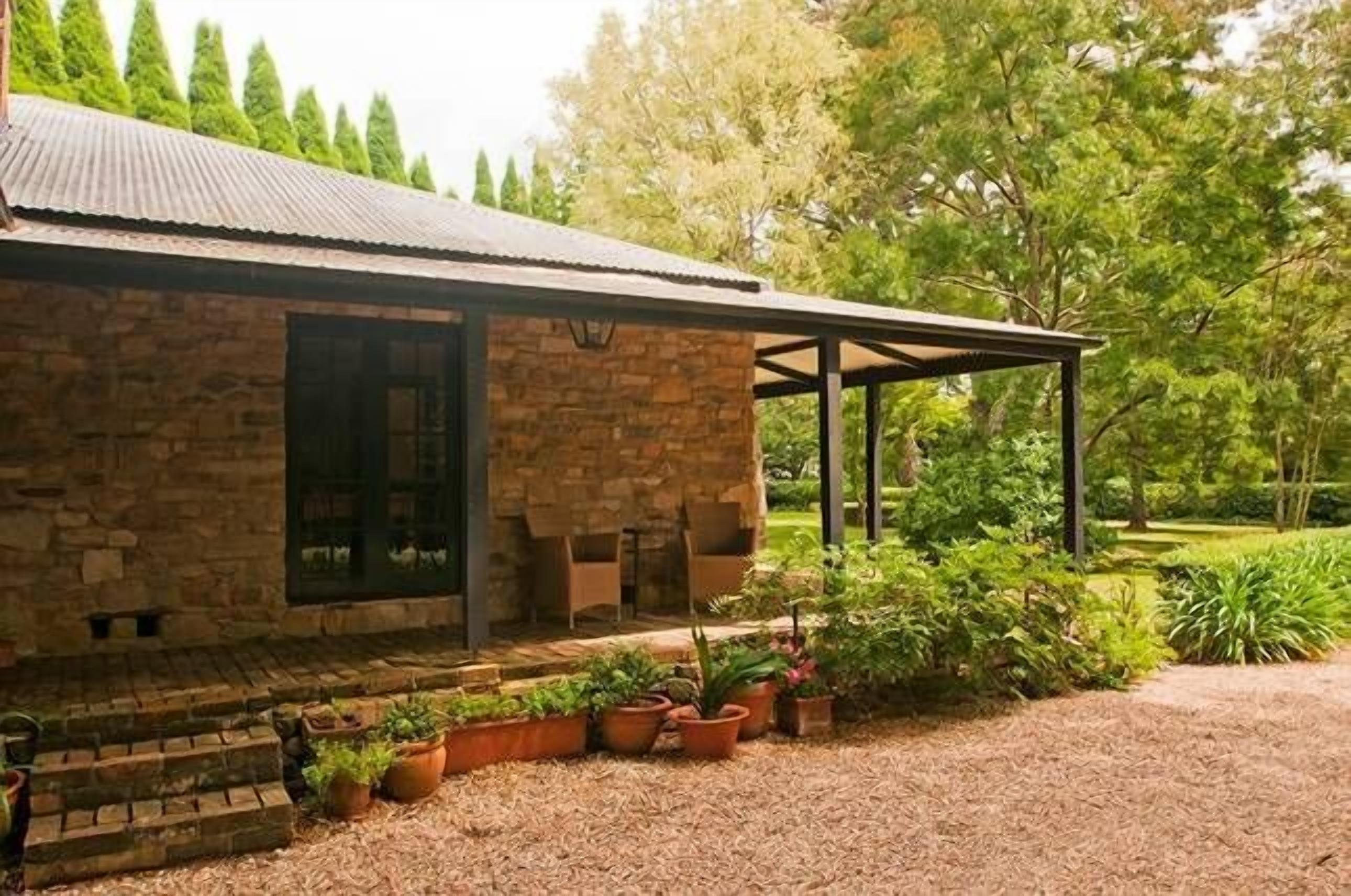 Un edificio de piedra con un patio cubierto, rodeado de plantas en macetas y un jardín bien cuidado.