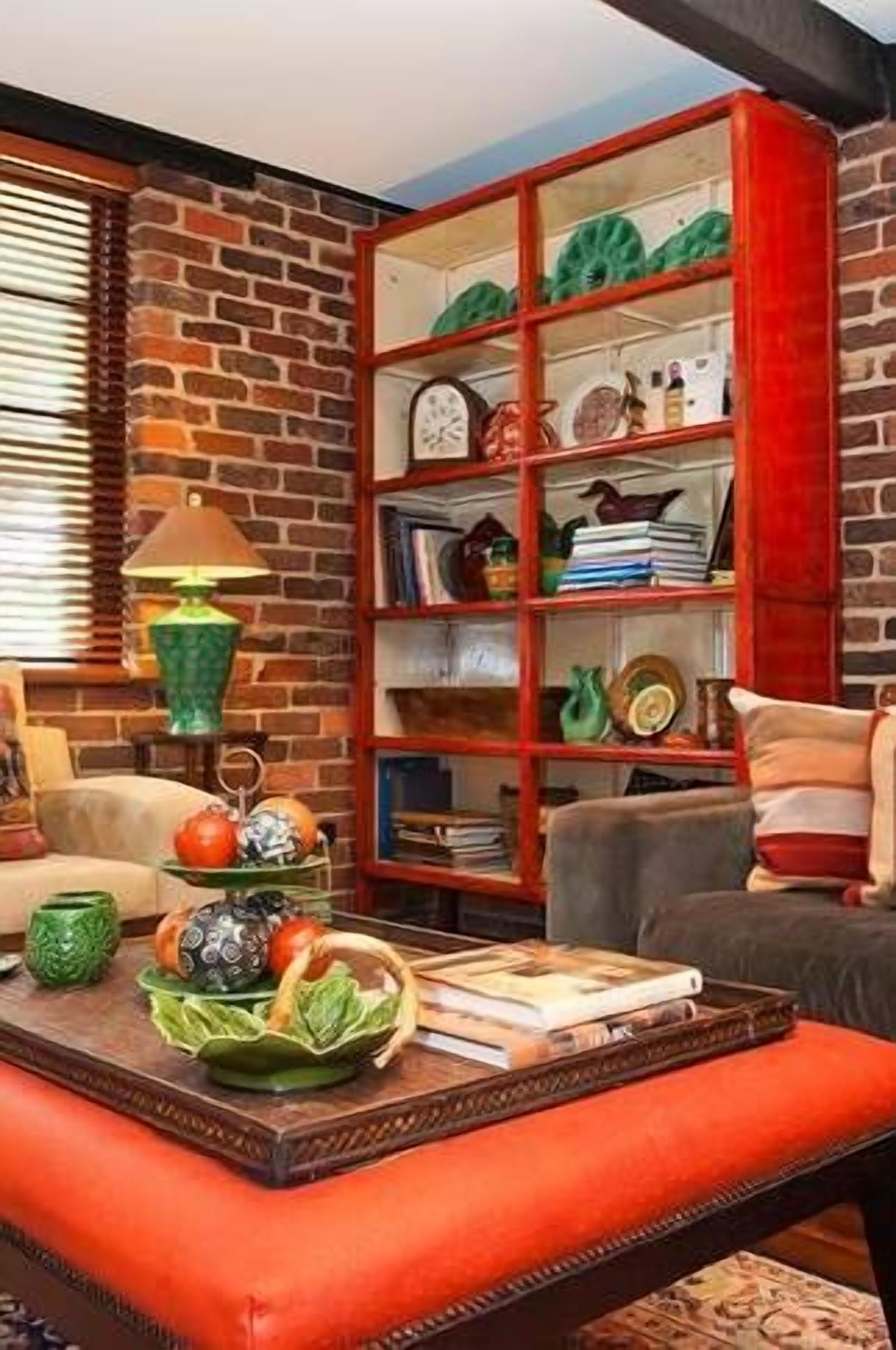 Een woonkamer met een bakstenen muur, een houten boekenkast, een bijzettafeltje met decoratieve objecten en een lamp.