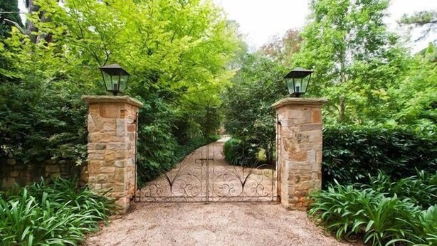 A gated entrance with stone pillars and a wrought iron gate, surrounded by lush greenery.