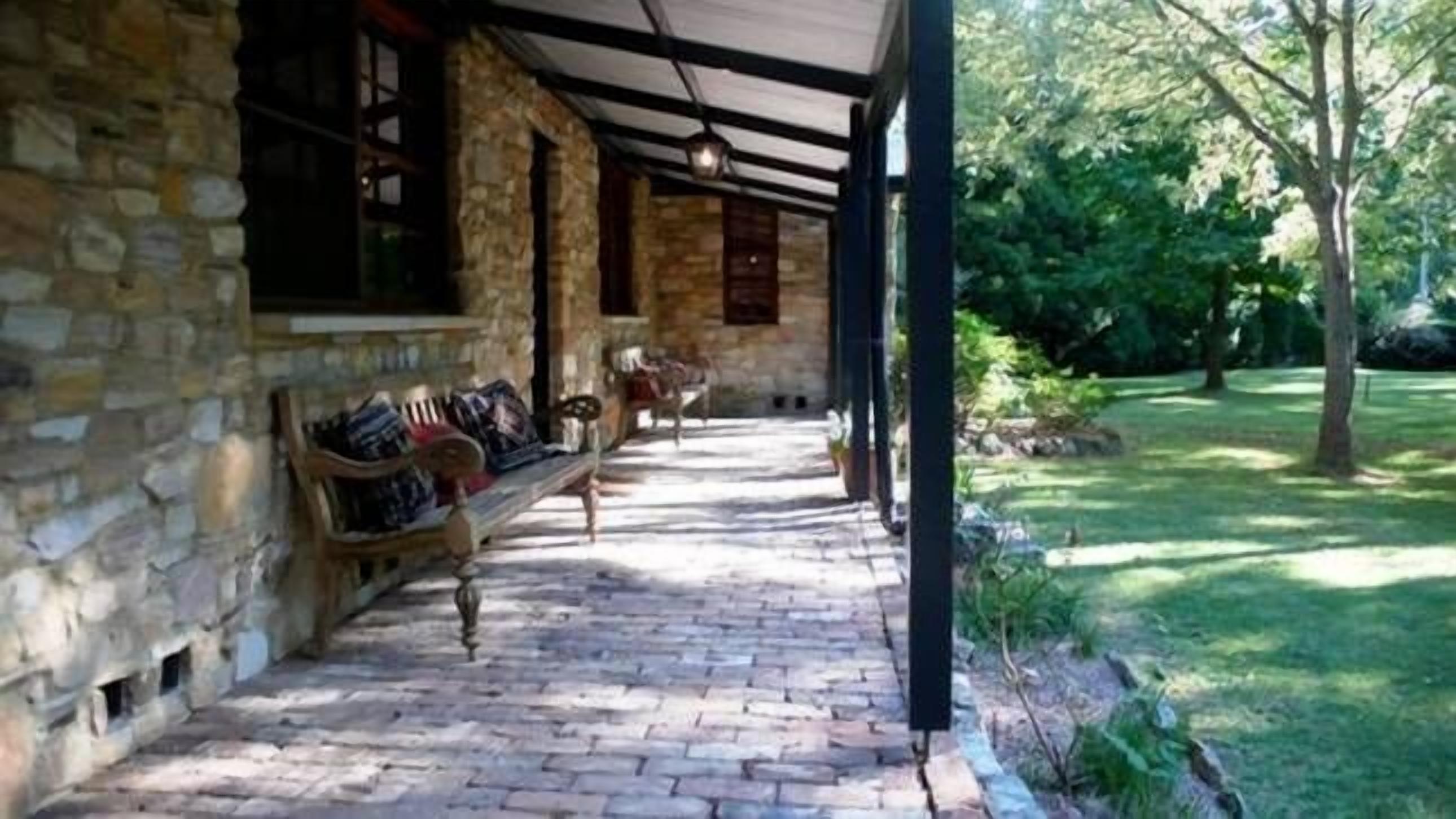 A stone building with a covered porch, a brick pathway, and a lawn with trees.