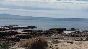 A rocky beach with clear water and distant mountains. - "The Old School House" (Currarong)