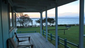 A covered porch with a view of the sea and a grassy area with a bench. - "The Old School House" (Currarong)