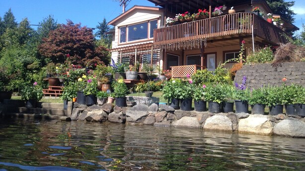 A two-story house with a balcony, surrounded by a garden with various potted plants and flowers.