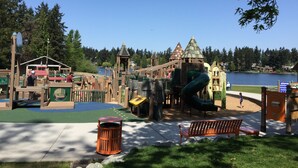 A playground with various play structures, a bench, and a trash can.