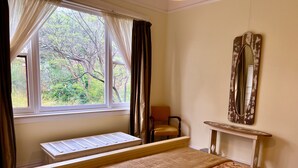 Quarto com cama, janela com cortinas, cadeira, espelho e uma mesinha.